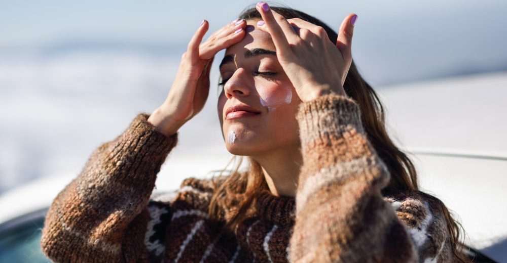 A woman applies sunscreen on her face while enjoying the outdoors, emphasizing winter skincare in Toronto.