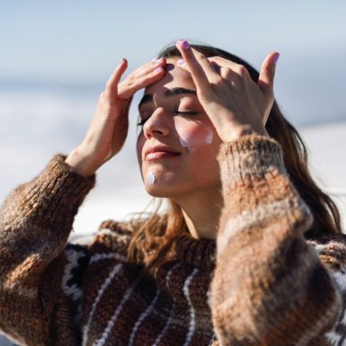 A woman applies sunscreen on her face while enjoying the outdoors, emphasizing winter skincare in Toronto.